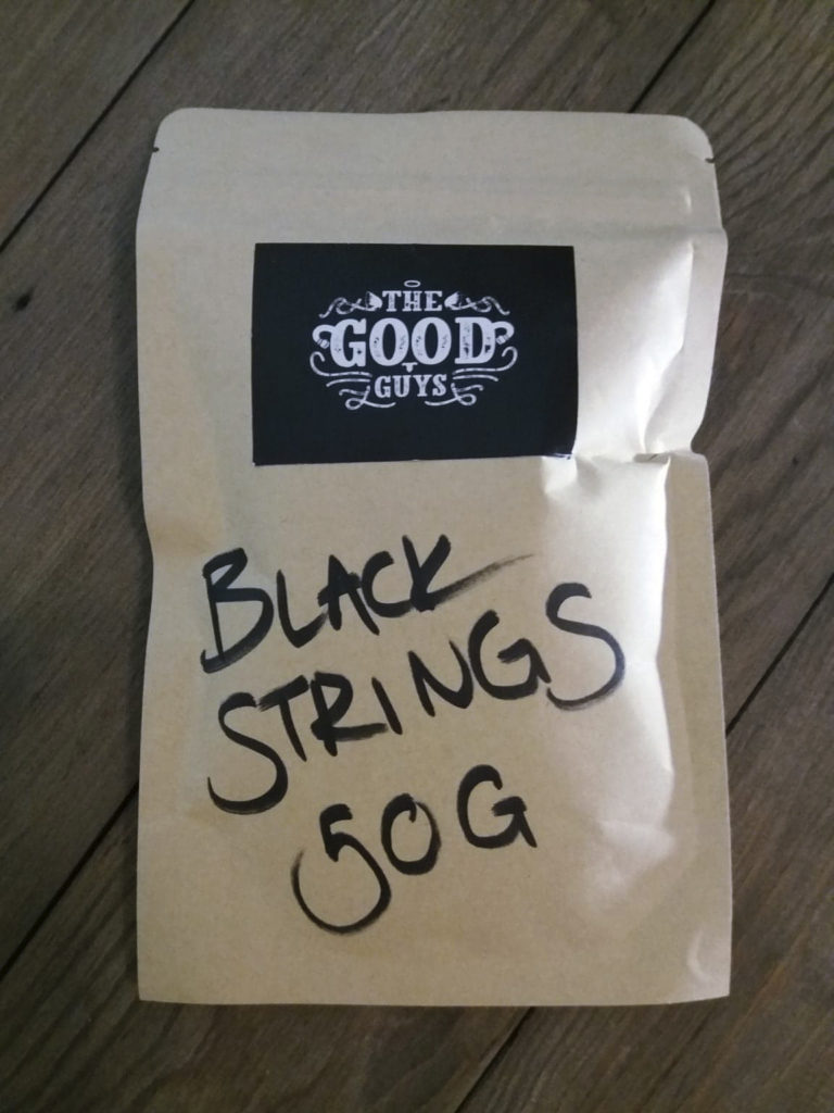 The Good Guys:ien maahantuomaa Black Strings -teetä valkoisessa pussissaan.