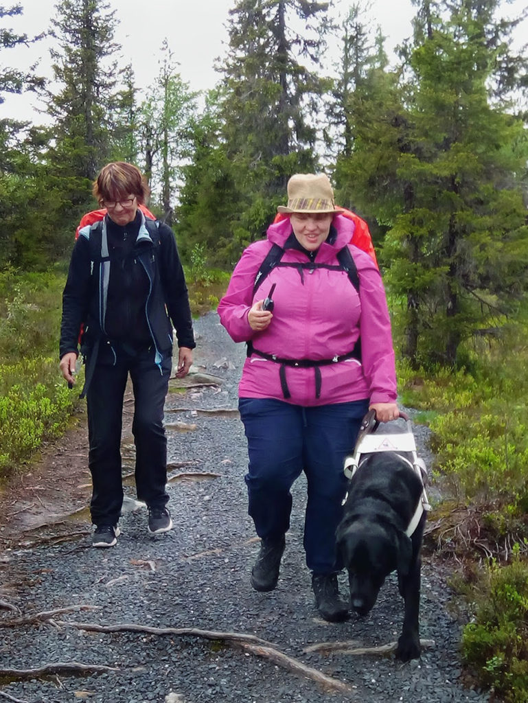 Sirpa ja Heidi sekä Otto kulkemassa juurten raidoittamaa ja kivituhkan peittämää polkua sekä harjoittelemassa radiopuhelinten käyttöä. Heidiltä se näyttää sujuvan hyvin. 