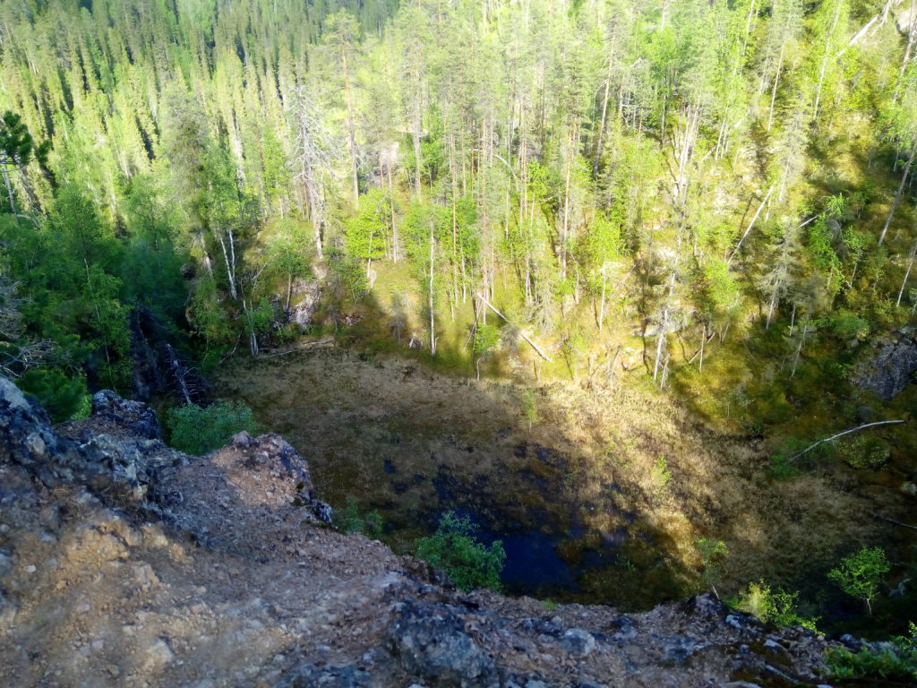 Huikaiseva näkymä pystysuoralta korkealta jyrkänteeltä alas laaksoon jossa suomaaston ympärillä kasvaa sankkaa metsää. 