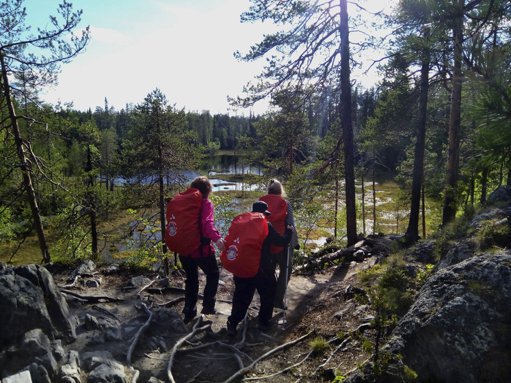 Taija, Outi ja Tuulikki vaikeakulkuisella juurien peittämällä polulla. Edessä kauniita syvänsinisiä suolampia. 