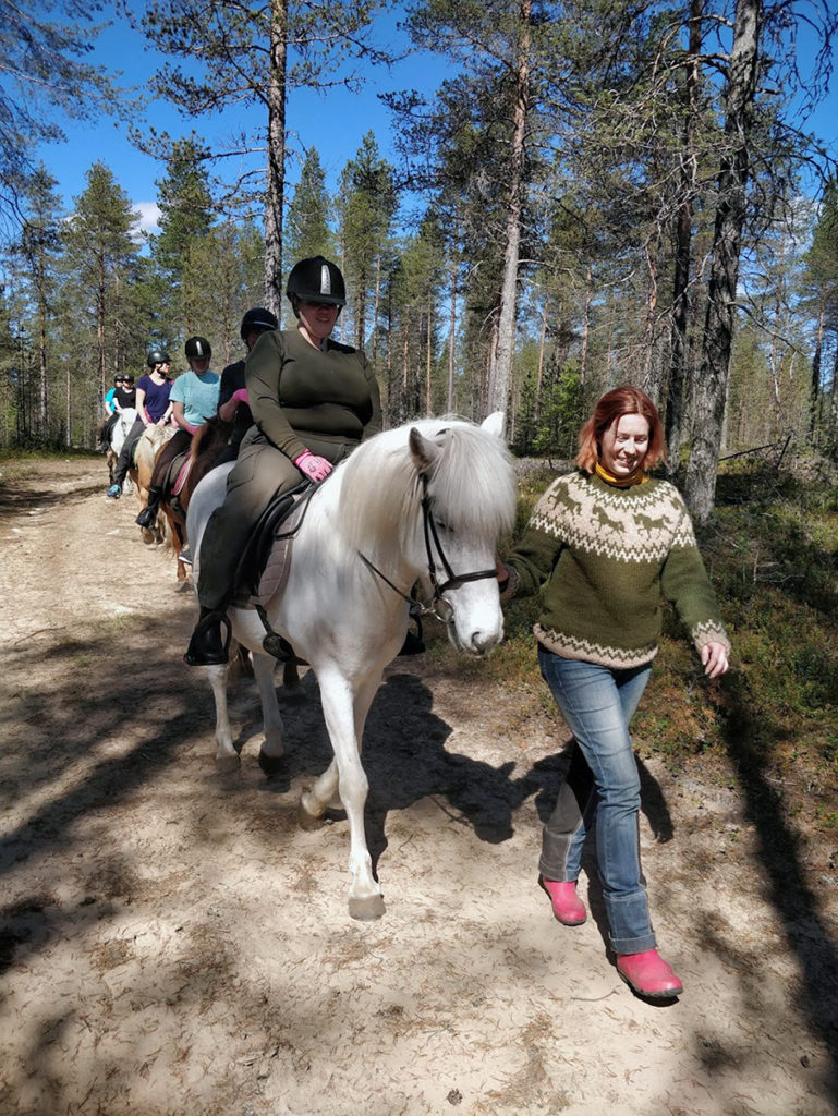 Seikkailijaryhmä ratsailla kauniissa aurinkoisessa kesäsäässä. Matka käy metsäautotietä letkassa Mirvan taluttaessa etummaisena kulkevaa Heidin hevosta. 